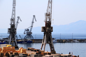 Old grey port cranes and small ships in the harbor in a sunny summer day in the city of Rijeka, with Ucka mountain and Istria peninsula in the background, Croatia, Europe