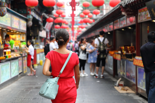 Woman tourist walking in chinatown on china travel. Asian girl on Wangfujing food street during Asia summer vacation. Traditional Beijing snacks being sold at chinese chinatown outdoor market.