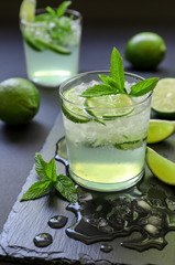 Cold cocktail with lemon liqueur, lime, tonic, ice on dark background.