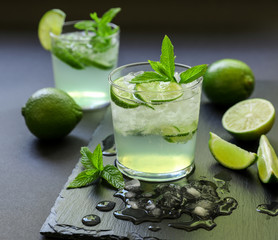 Cold cocktail with lemon liqueur, lime, tonic, ice on dark background.