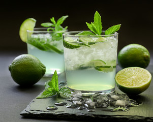 Cold cocktail with lemon liqueur, lime, tonic, ice on dark background.