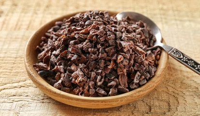 Bowl with aromatic cocoa nibs on wooden table