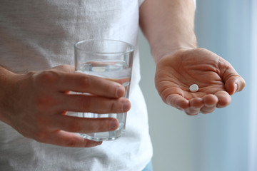 Young man with pill and glass of water, closeup