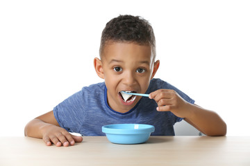 Cute African American boy eating yogurt on white background