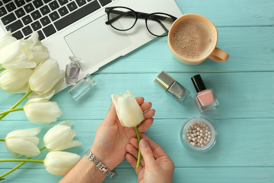 Female hands holding white tulip on table with computer, cosmetics, glasses and cup of coffee