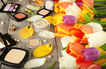 Composition of colorful flowers and cosmetics on wooden table