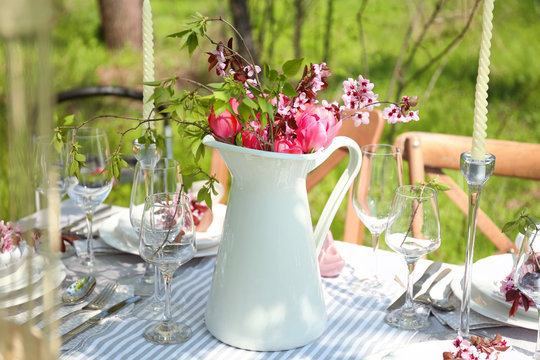 Jug with blooming bouquet of flowers on served table in garden