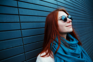 Hipster redhaired girl in stylish sunglasses is posing in front of a black wall on the street