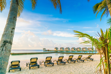 Beach chairs in Maldives island with water villas at the sunrise time .