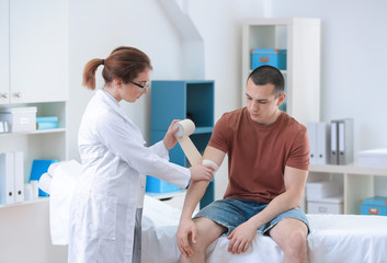 Obraz premium Orthopedist applying bandage onto patient's arm in clinic