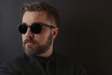 Fototapeta premium A brutal man with a beard and a stylish hairdo in a black suit and sunglasses