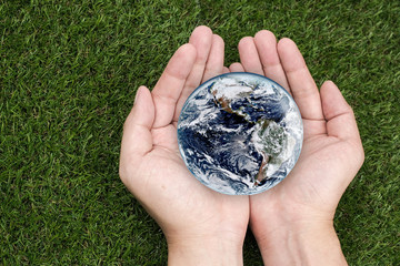Hands holding earth on green grasses. Elements of this image furnished by NASA