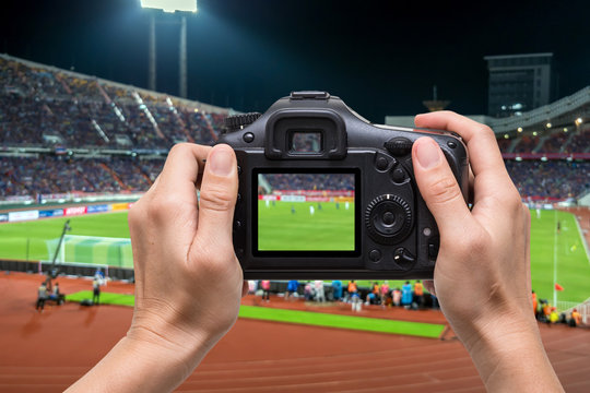 Hand holding the camera over blurred of action photographer taking photo at player in Abstract blurred photo of soccer stadium, sport background concept