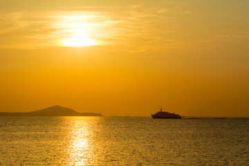 passenger boat with orange sunset and silhouette shoreline reflecting glows in water surface