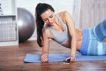 Slim fitness young woman doing exercise at home with smartphone