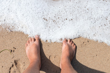 Legs of person on a sand. Legs of a man standing on the sand ion the beach from above. Horizontal outdoors shot. Bali island.