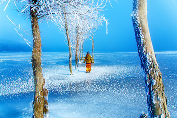 Woman on ice lake in beautiful ethno dress and beautiful frozen trees.