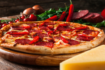 Cuisine italienne appétissante. Pizza cuite au four avec salami, piment, tomates et fromage servie sur fond rustique en bois avec des ingrédients.