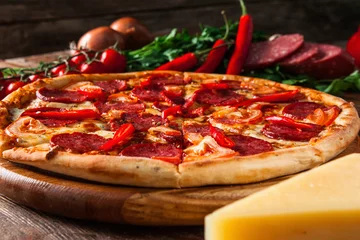 Cercles muraux Pizzeria Cuisine italienne appétissante. Pizza cuite au four avec salami, piment, tomates et fromage servie sur fond rustique en bois avec des ingrédients.