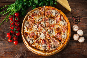 Pizza au jambon, fromage et champignons, servie sur fond de bois rustique avec tomates cerises, persil et grains de poivre, mise à plat. Photo de cuisine italienne.