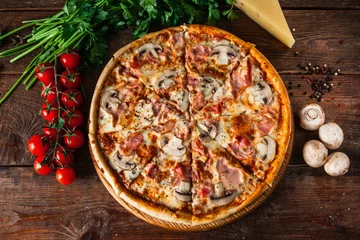 Crédence de cuisine en verre imprimé Pizzeria Pizza au jambon, fromage et champignons, servie sur fond de bois rustique avec tomates cerises, persil et grains de poivre, mise à plat. Photo de cuisine italienne.