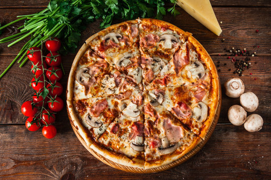 Pizza with ham, cheese and mushrooms, served on rustic wooden background with cherry tomatoes, parsley and peppercorns, flat lay. Italian cuisine photo.