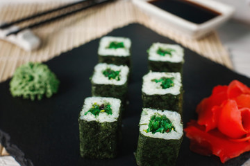 Delicious sushi rolls set served on black slate with ginger and wasabi. Japanese healthy vegetarian food, closeup.