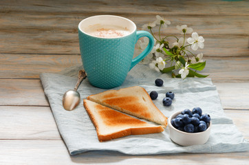 Breakfast idea. Cup with coffee with blueberries, cherry blossom and toast on linen napkin and wooden background