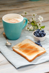 Breakfast idea. Cup with coffee with blueberries, cherry blossom and toast on linen napkin and wooden background