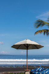 Beach umbrella on a sunny day, sea in background. Tropical beach with black sand. Beautiful sky. Paradise island Bali, Indonesia.