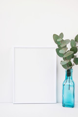 Frame mockup on white background, green eucalyptus branch in blue glass bottle, copyspace for text, styled image