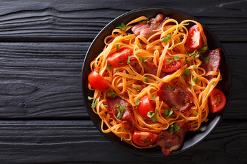 Carrot noodles with bacon and tomatoes close-up. horizontal top view