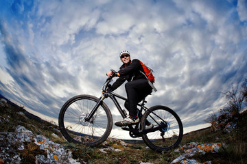 Fototapeta na wymiar Portrait of the mountain cyclist standing with bike on the rocky hill against dramatic sky with clouds.