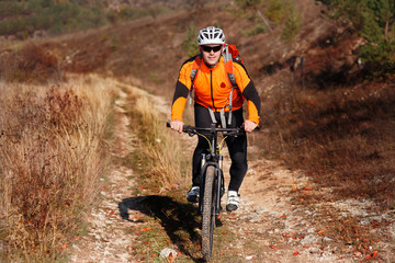 Cyclist in the orange jacket riding the bike on the beautiful summer mountain trail.