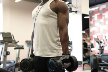 Fototapeta na wymiar Muscular black man in a white t-shirt doing exercises with dumbbells at gym