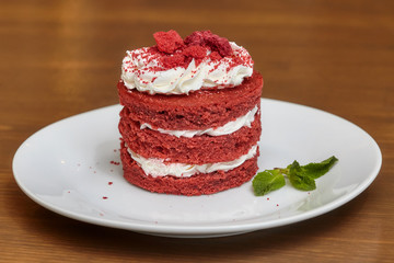 Red velvet cake with cream on white plate, wooden table