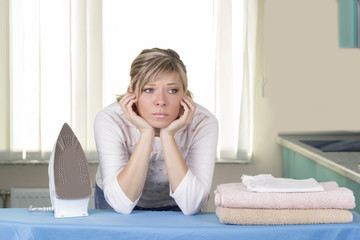 Lazy up housewife sitting amongst her clean laundry piled on the ironing board daydreaming