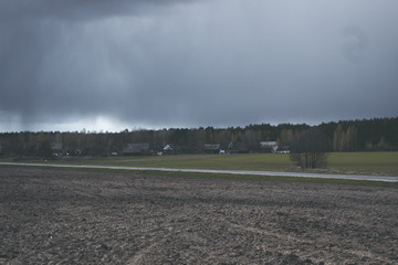 Rain cloud over the village in the spring. Gray road. Europe
