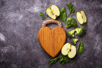 Green food background with wooden board in shape of heart
