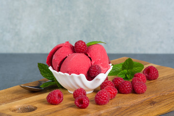 Raspberry ice cream sorbet in white porcelaine bowl with raspberry, mint leaves  copy space on wooden plank and grey textured background