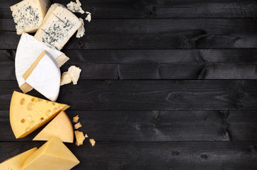 Different types of cheese on black wooden table. Top view