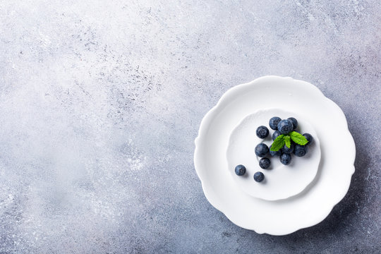 Freshly picked blueberries on white plate on gray stone background. Concept for healthy eating and nutrition with copy space. Top view.