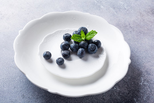 Freshly picked blueberries on white plate on gray stone background. Concept for healthy eating and nutrition with copy space.