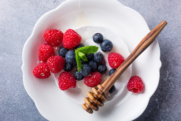 Freshly blueberries and raspberries on white plate with honey. Healthy eating and nutrition concept with copy space. Top view.