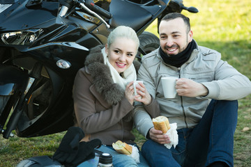 couple posing near motor bike with sandwitches and coffee