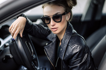 Fototapeta na wymiar fashion outdoor photo of sexy beautiful woman with dark hair in black leather jacket and sunglasses posing in luxurious auto