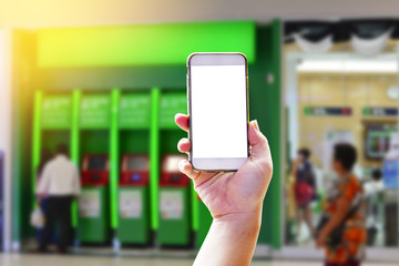 Female hand holding a smartphone with blank screen on blur Automatic Teller Machine or ATM of branch bank for use mobile internet banking replace queue line in the bank