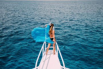 woman on yacht nose with blue scarf wave on wind. summer time vocation on yacht.