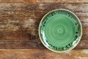 Top view of green empty ceramic plate on wooden background with copy space.