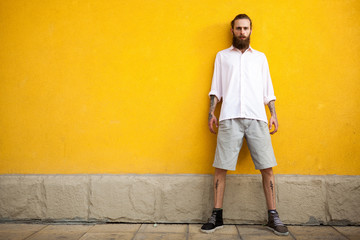 Obraz na płótnie Canvas Cool Tattooed bearded hipster on yellow wall posing outdoor